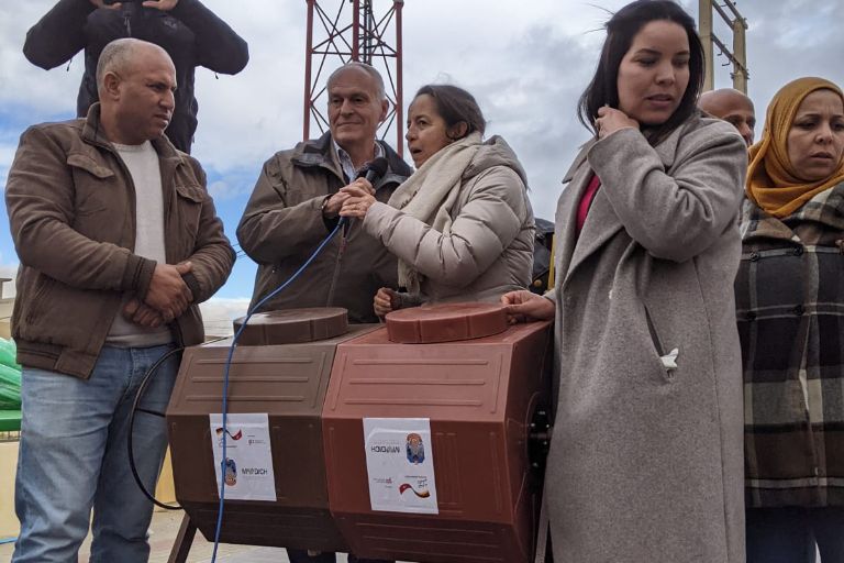 Mehrere Menschen stehen auf einer kleinen Bühne um einen Komposter und erklären ihn
