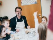 Stadtschulrat Florian Kraus sitzt mit Schürze mit mehreren Kindern an einem Tisch und isst gemeinsam mit ihnen in einer Betreuungseinrichtung.