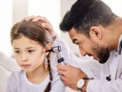 Ein Arzt steckt ein ärztliches Untersuchungsinstument in das Ohr eines Mädchens.