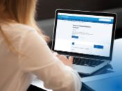 Das Bild zeigt eine Frau von hinten am Laptop sitzend und schreibt auf der Tastatur