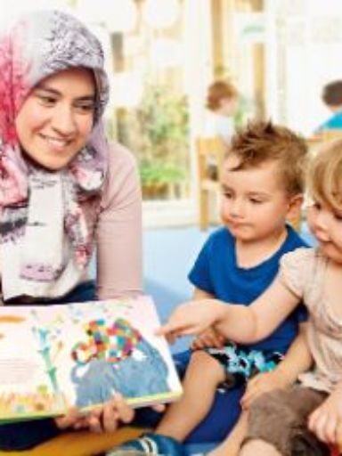 Erzieherin liest kleinen Kindern aus Bilderbuch vor