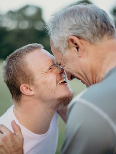 Behinderter Junge scherzt und lacht mit einem Mann ohne Behinderung