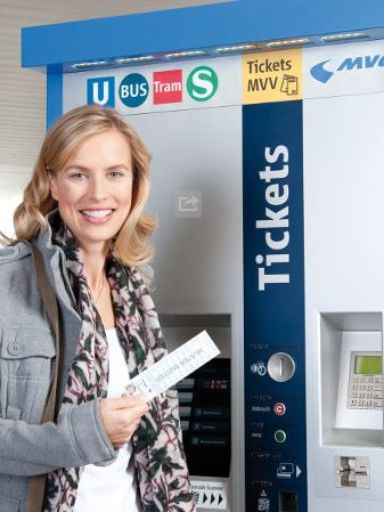 Frau steht vor Ticketschalter und hält ein Ticket in der Hand. 