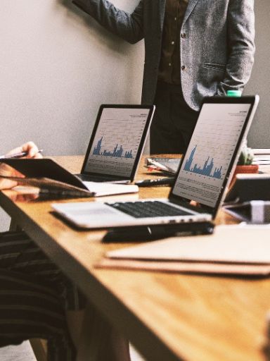 Menschen sitzen in einem Meeting um einen Tisch mit Laptops und Akten.