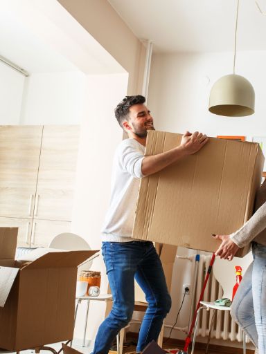 Ein junges Paar trägt einen Umzugskarton in eine Wohnung